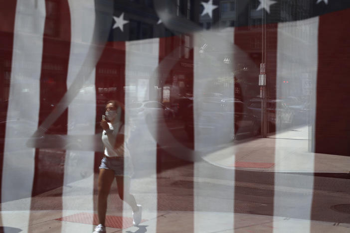 A passerby wears a mask out of concern for the coronavirus while walking past an American flag displayed in Boston on Tuesday. The U.S. has now recorded more than 3 million confirmed cases of the coronavirus.
