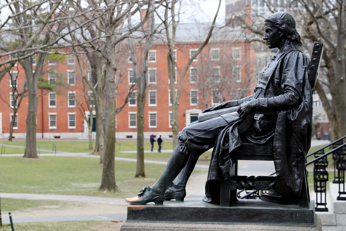 A statue of John Harvard, namesake of the university, overlooks the campus earlier this year. Harvard University joined the Massachusetts Institute of Technology in suing the federal government over its policies on international students Wednesday.