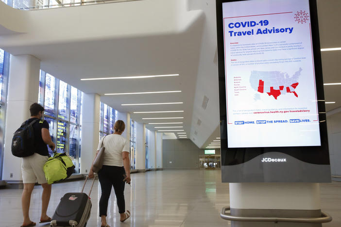 Arriving travelers walk by a COVID-19 travel advisory sign in the baggage claim area at New York City's LaGuardia Airport. New York state is requiring travelers from states on its quarantine list to show proof that they've completed a form with their contact information.