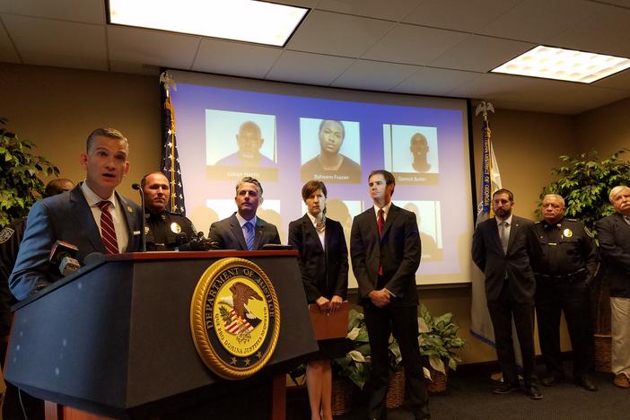 U.S. Attorney Bobby Christine announces charges against 30 Savannah residents following an investigation of two rival gangs. Behind him are photos of the six suspects still at large.