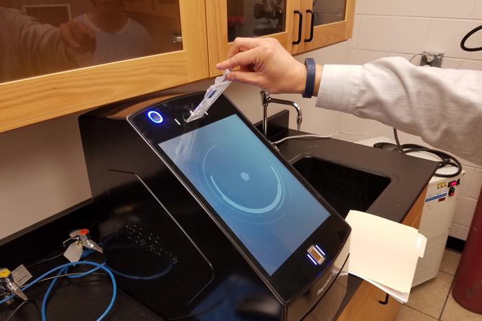 Professor Kai Shen demonstrates how DNA samples are inserted into the machine for rapid analysis.