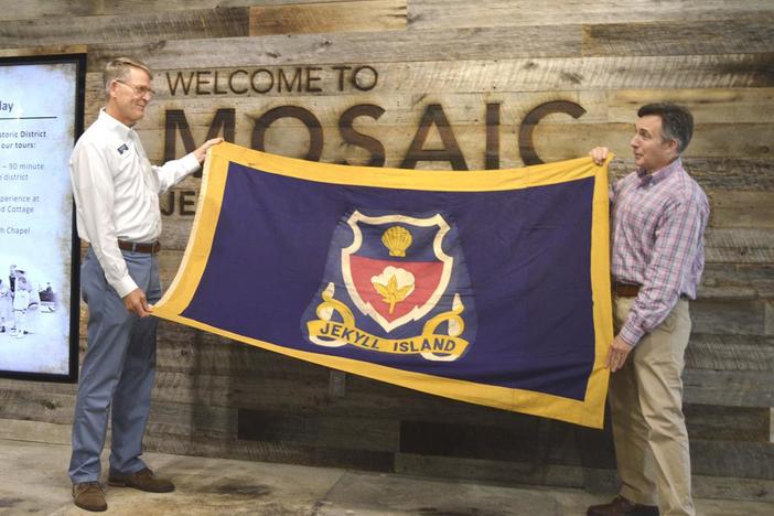 Buff Leavy, right, president and executive editor of Brunswick News Publishing Co., presents Jekyll Island's long-lost official flag to Jekyll Island Authority Executive Director Jones Hooks at the Mosaic museum on the island. 