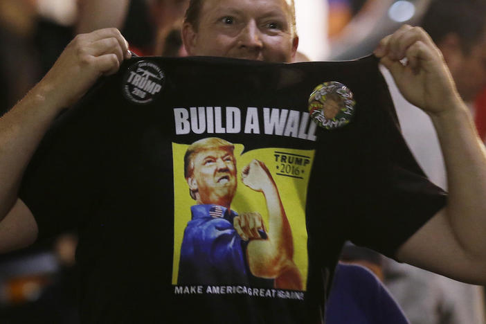 A supporter of Republican presidential candidate Donald Trump holds up his shirt, which bears the Trump slogan "Build a Wall," following a rally for Trump, Tuesday, Aug. 30, 2016, in Everett, Wash.