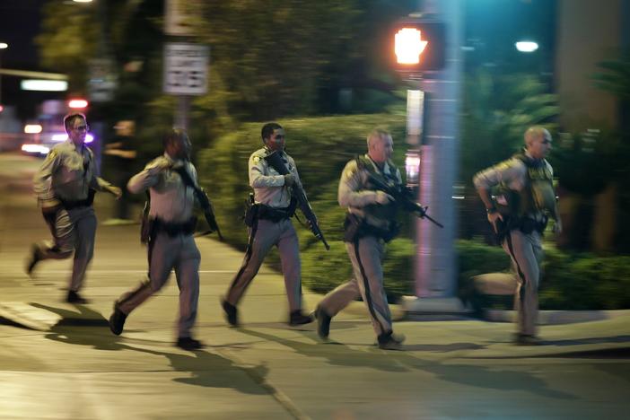 Police run to cover at the scene of a shooting near the Mandalay Bay resort and casino on the Las Vegas Strip, Sunday, Oct. 1, 2017, in Las Vegas.