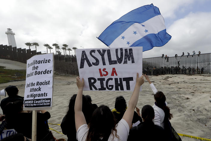 Central American migrants sit on top of the border wall on the beach in San Diego during a gathering of migrants living on both sides of the border.