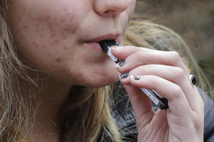 A high school student uses a vaping device. 