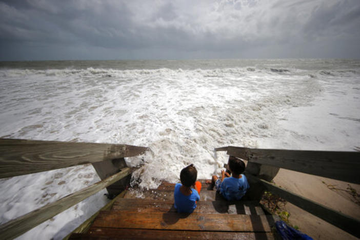 Maximus Modert, left, and Tyde Modert, of Fort Pierce, Fla., sit on boardwalk steps at the edge of a high surf from the Atlantic Ocean, in advance of the potential arrival of Hurricane Dorian, in Vero Beach, Fla., Monday, Sept. 2, 2019.