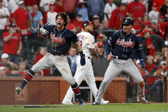 Atlanta Braves' Dansby Swanson, left, and Rafael Ortega, right, celebrate after scoring as St. Louis Cardinals relief pitcher Carlos Martinez (18) walks in the background during the ninth inning in Game 3 of a baseball National League Division Series.
