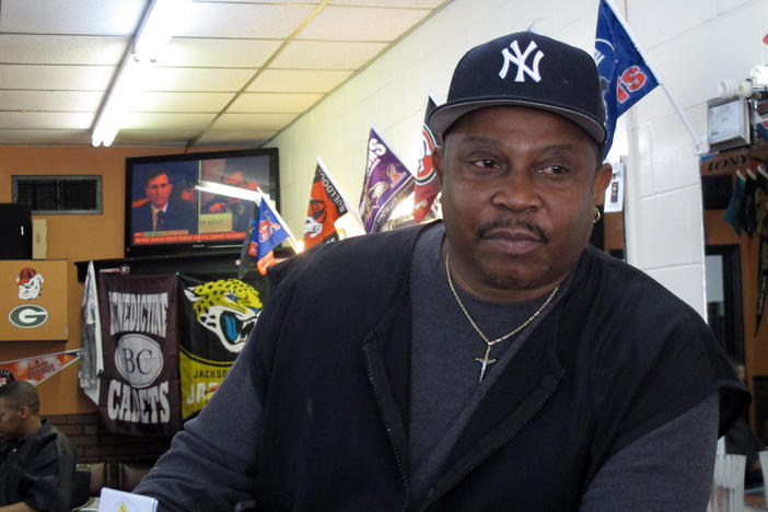 Anthony Harris sits inside his barber shop in Savannah, while a live broadcast of the Congressional impeachment hearing plays on television. Harris said he believes President Trump should be removed from office but he's tired of the coverage.