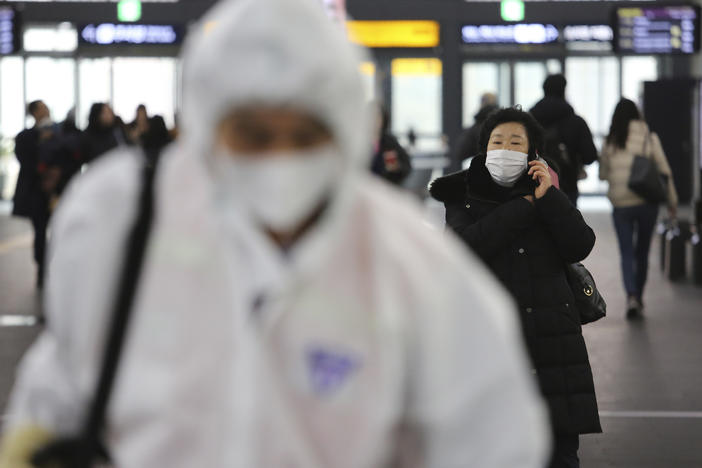 A woman wears a mask as an employee works to prevent a new coronavirus at Suseo Station in Seoul, South Korea, Friday, Jan. 24, 2020.
