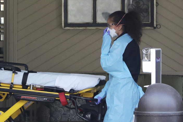 An ambulance worker adjusts her protective mask as she wheels a stretcher into a nursing facility where more than 50 people are sick and being tested for the COVID-19 virus, Saturday, Feb. 29, 2020, in Kirkland, Wash.