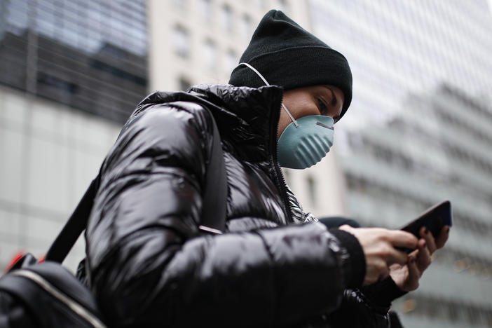 A woman uses her phone while wearing a face mask in New York City. With so many people searching for information on coronavirus, cybersecurity experts warn that it has provided new channels for phishing and malware attacks.