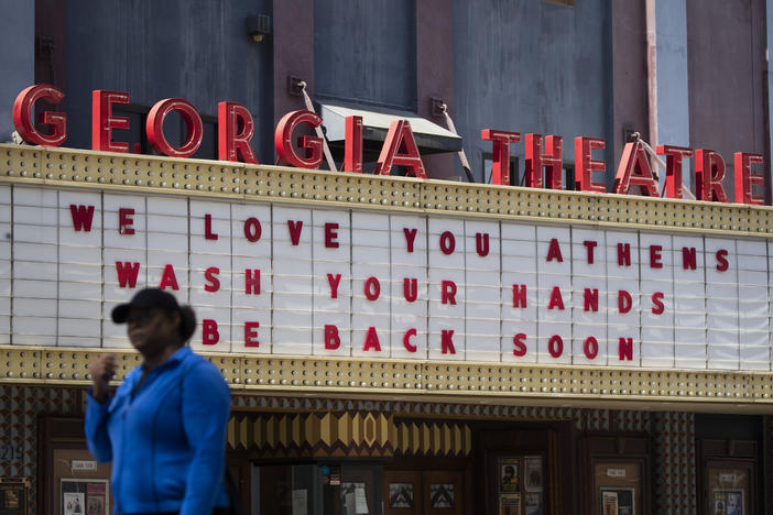 A woman walks past the Georgia Theatre Friday, March 20, 2020, in downton Athens, Ga. A note posted on the theatre's door says they are closed and all shows are postponed. 