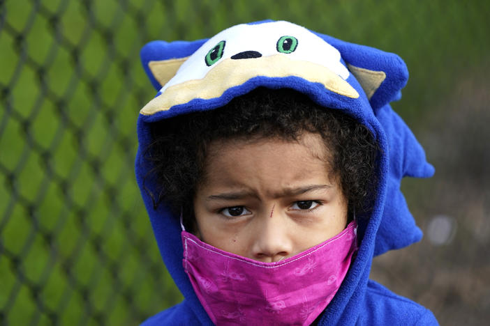 A child wears a mask while waiting for food at an emergency distribution center in Texas. Gwinnett and Cobb counties announced Friday a shift to four days a week digital learning for the remainder of the school year. 