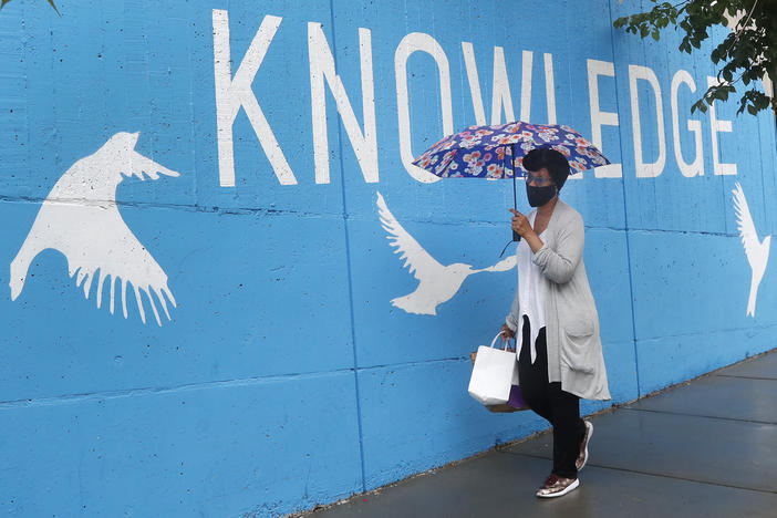 A woman wearing a mask due to coronavirus concerns walks by a public library, Tuesday, June 30, 2020, in Cambridge, Mass. 