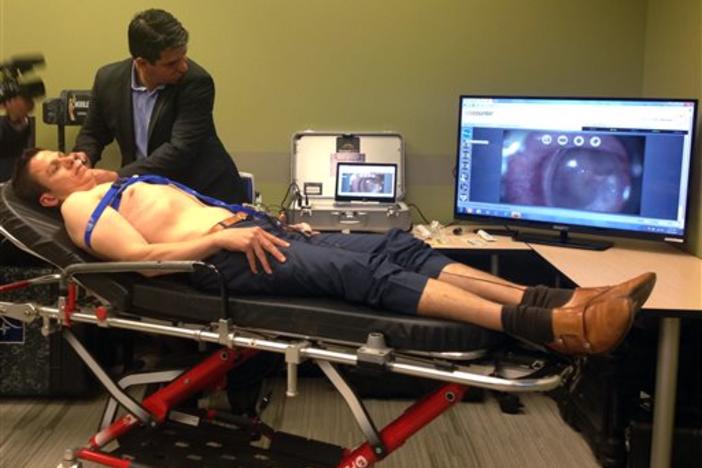 Manoel Coelho, a GlobalMed representative, uses a device with a camera to look at colleague Tim White's ear, displayed on monitor, during a June 22, 2015, demonstration of some of the technology and equipment options available for telehealth services. 