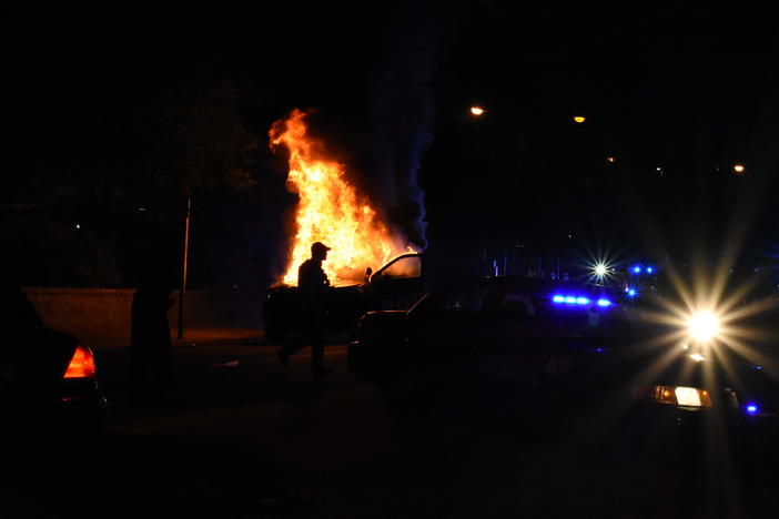 A police officer stands guard in front of a burning Georgia Tech police vehicle. Masked protesters threw a flare into the car.
