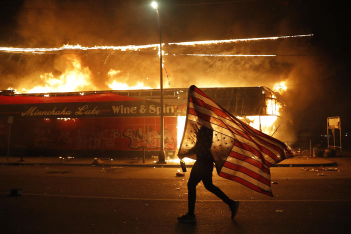 A protester carries a U.S. flag next to a burning building Thursday in Minneapolis. Protests over the death of George Floyd, a black man who died in police custody Monday occured for several days.