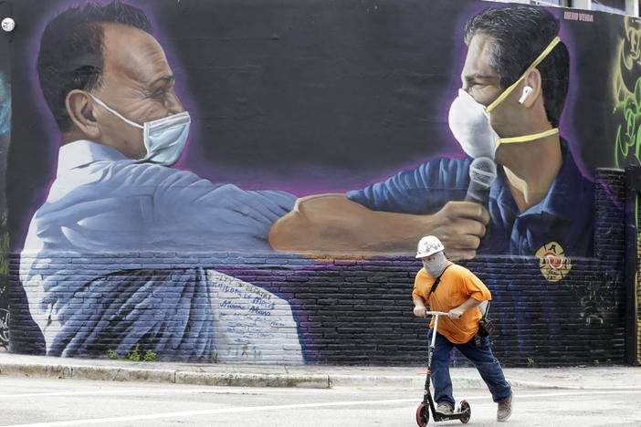 A construction worker rides a scooter Monday in Miami past a Hiero Veiga mural of businessman Moishe Mana (left) and Miami Mayor Francis X. Suarez wearing masks.