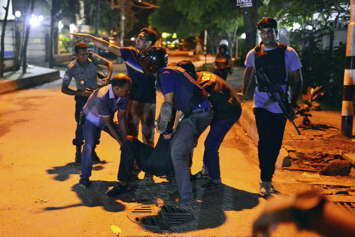 People help an unidentified injured person after a group of gunmen attacked a restaurant popular with foreigners in a diplomatic zone of the Bangladeshi capital Dhaka, Bangladesh, Friday, July 1, 2016.