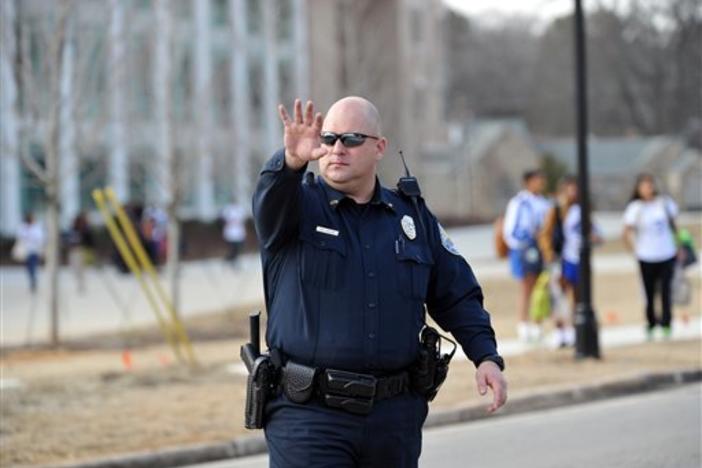 A police officer stops traffic in front of Chamblee Charter High School after a youth was arrested for carrying loaded guns, according to authorities, on Tuesday, Feb. 18, 2014, in Chamblee, Ga.