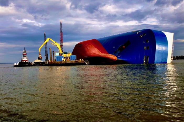A knuckle boom excavator picks up 1-to-3-inch rock-aggregate from a container barge in St. Simons Sound. The excavator guided by sonar and GPS, strategically places the rock next to the hull of the M/V Golden Ray to slow erosion.