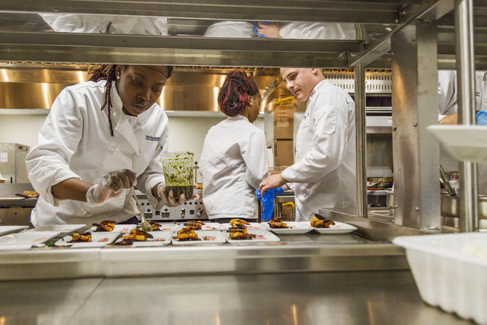 Hutchins College and Career Academy student Shanitra Rooks plates up course two our of four, in this case grilled shrimp with black rice, under the watchful eye of Chef Stuart Hardy. Hardy, a former executive chef, runs the eight month old program.