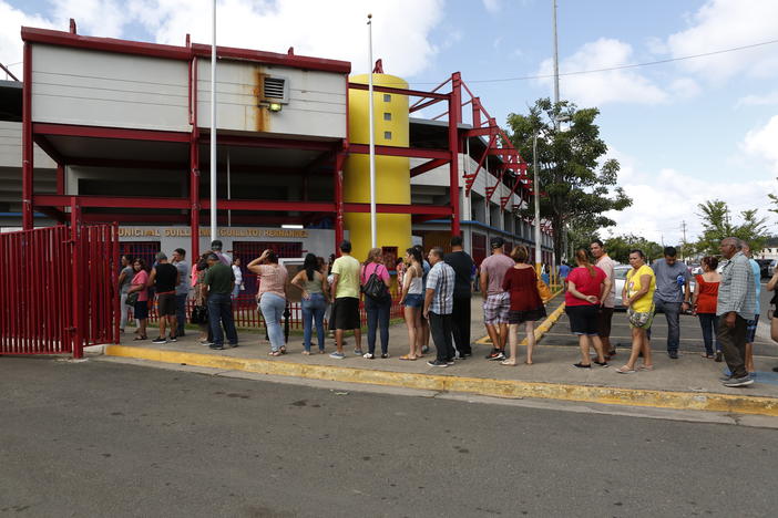 People in Aguada, Puerto Rico line up at a distribution center running out of the municipal baseball stadium. The center receives food aid from FEMA contractors and other private donations.