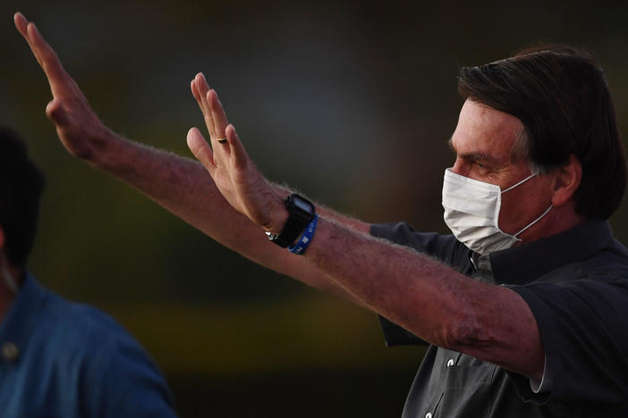 Brazilian President Jair Bolsonaro waves to supporters from the Alvorada Palace in Brasilia on Monday, the same day that two more of his Cabinet ministers were diagnosed with COVID-19.