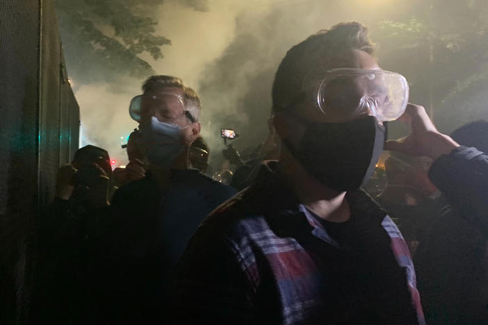 Mayor Ted Wheeler (in dark shirt at left) stands at a fence outside the Mark O. Hatfield U.S Courthouse in Portland, Ore., as federal officers deploy tear gas Wednesday night. People protesting police violence and systemic racism have faced tear gas, impact munitions and other dispersal tactics by the Portland Police Bureau and federal law enforcement.
