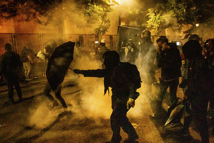 Protesters walk through chemical irritants deployed by federal agents in Portland, Ore. The Justice Department inspector general says he is investigating federal officers' roles in responding to protests in Portland and Washington, D.C.