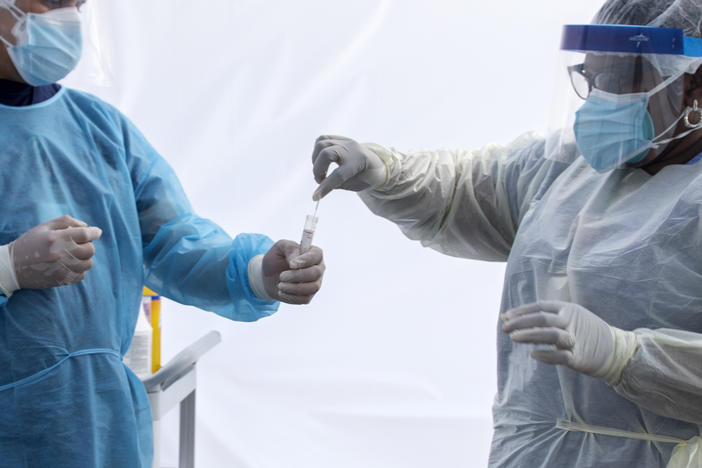 A health worker puts a nasal swab sample into a tube in a tent at a COVID-19 testing site at St. John's Well Child and Family Center in Los Angeles.