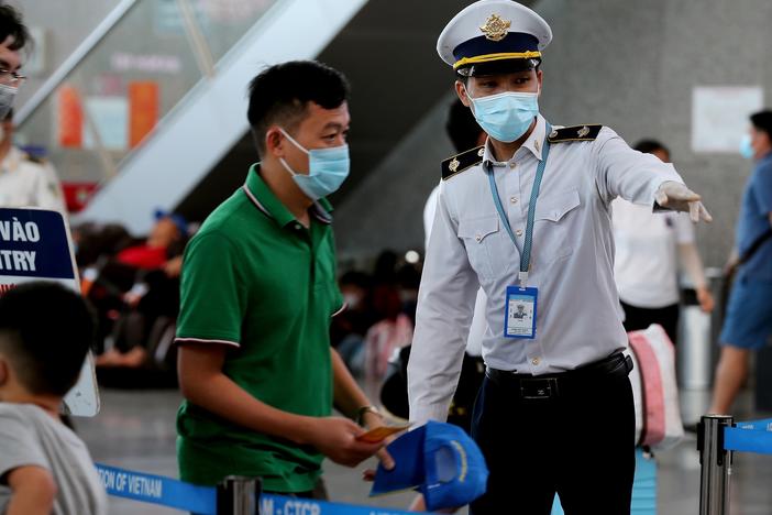 A staff member from Vietnam's disease control authority assists passengers as they queue up for temperature checks at the departure terminal at Da Nang's international airport on Monday.