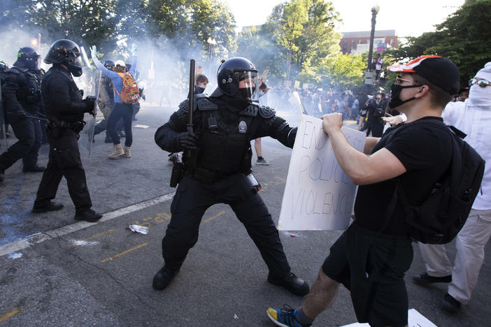 A law enforcement officer raises a baton and tear gas is fired during protests near the White House on June 1.