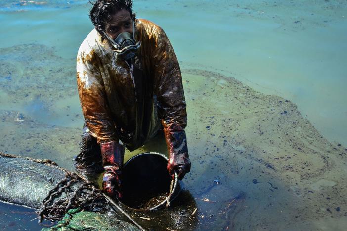 A man scoops oil from the coast of Mauritius on Saturday. A Japanese cargo ship ran aground near Blue Bay Marine Park in late July and began to leak fuel oil and diesel into pristine waters.