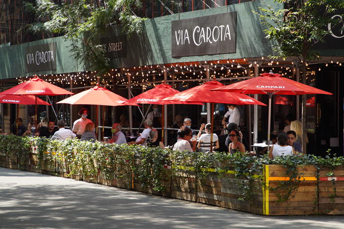 People dine under red umbrellas outside Via Carota restaurant in New York City's West Village. As the city continues to reopen, it is allowing restaurants to expand outdoors.