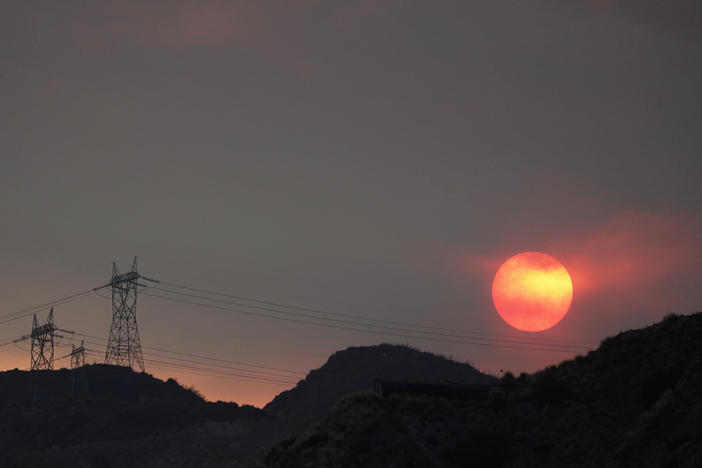 The sun sets through smoke created by the Ranch Fire on Aug. 13, 2020, in Azusa, Calif. A heat wave has prompted electrical providers to issue the first rolling blackouts in the state since 2001.