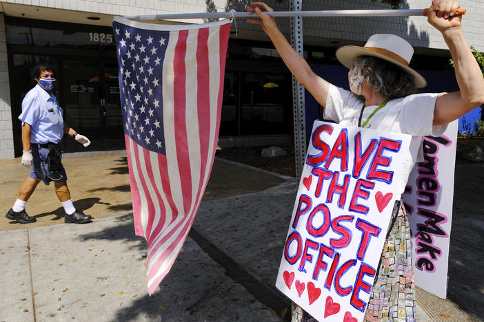 Erica Koesler of Los Angeles demonstrates outside a USPS post office as a postal worker walks by in the background on Saturday. The USPS has warned states coast to coast that it cannot guarantee all ballots cast by mail for the November election will arrive in time to be counted, even if mailed by state deadlines.