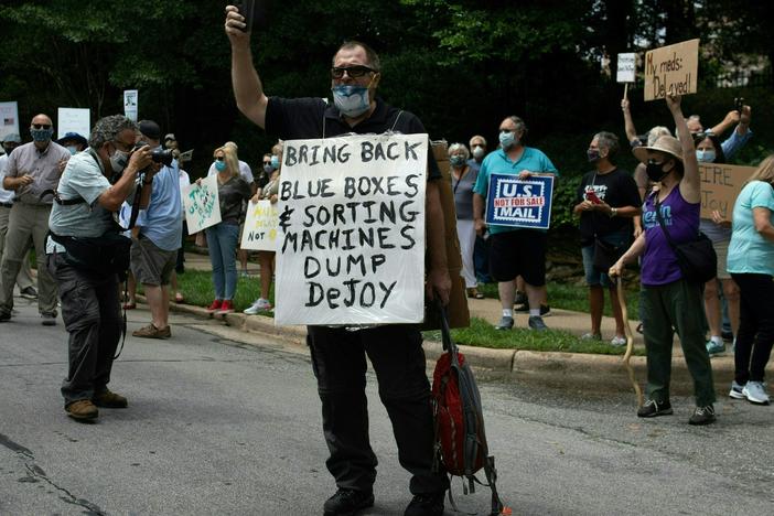 A group of protestors holds a demonstration in front of Postmaster General Louis DeJoy's home in Greensboro, N.C. on Sunday. DeJoy has recently come under fire for changes made at the U.S. Postal Service that have delayed mail in advance of the November elections.