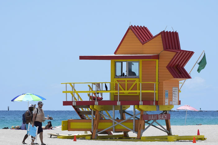Beachgoers walk past a lifeguard tower on a nearly empty beach on Aug. 11 in Miami Beach, Fla.