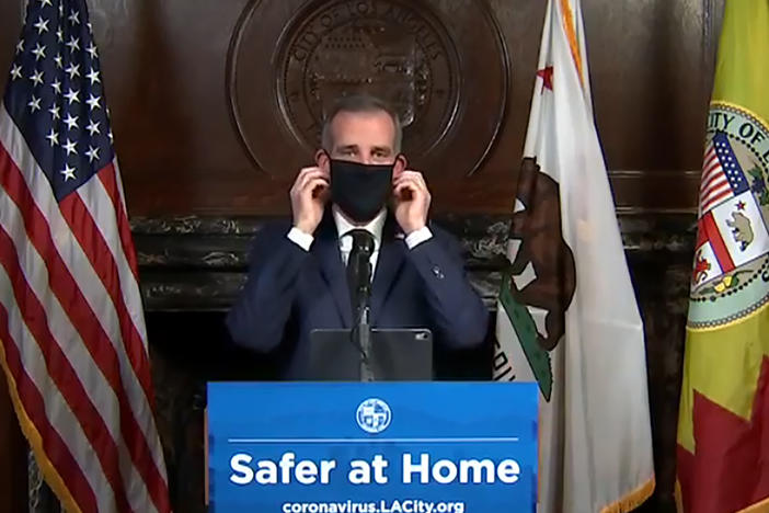 Los Angeles Mayor Eric Garcetti puts on a face mask during a news briefing in April.