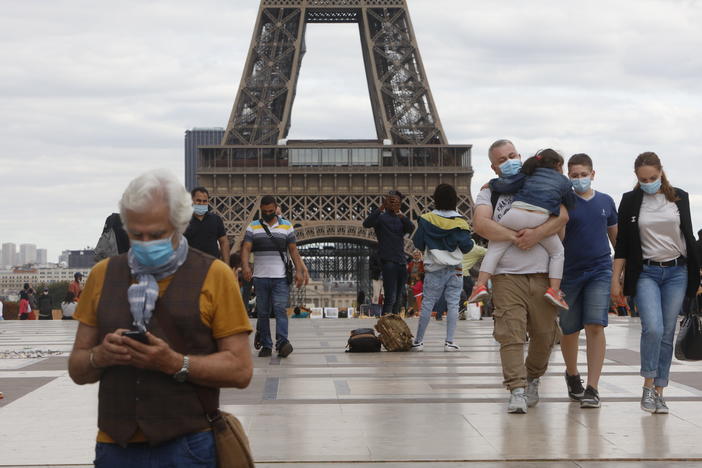 People wearing masks walk near the Eiffel Tower in Paris on Thursday, the same day that the government made masks mandatory in all the city's public outdoor spaces.