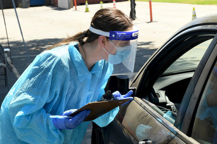 An urgent care worker wears personal protective equipment in drive-up testing for the coronavirus in the Los Angeles area. Leading public health scientists tell journalist Alexis Madrigal that widespread at-home testing could help contain the virus.