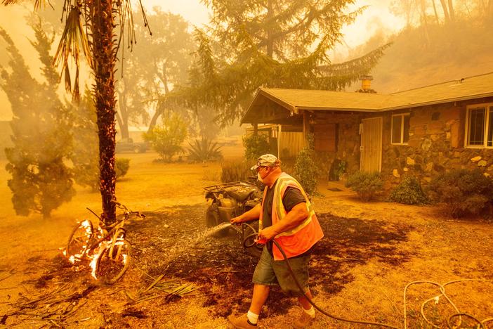 A Californian resident hoses down a burning bicycle and tree as flames from the Hennessey Fire approach a property in the Spanish Flat area of Napa, Calif., on Aug. 18.