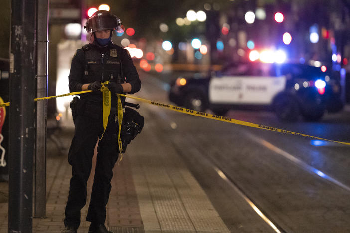 A Portland police officer ties a police line around the scene of a fatal shooting in Portland Saturday. It's the latest incident after weeks of Trump supporters clashing with counterprotesters.