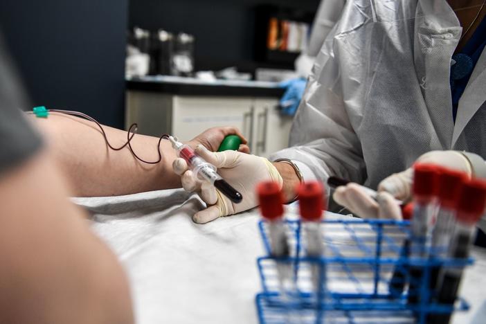 A researcher takes blood samples from a patient as she participates in a COVID-19 vaccine study last month at the Research Centers of America in Hollywood, Fla.