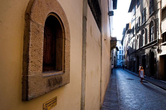 A girl walks past a <em>buchetta del vino</em>, a small window to serve wine, typical in Florence.