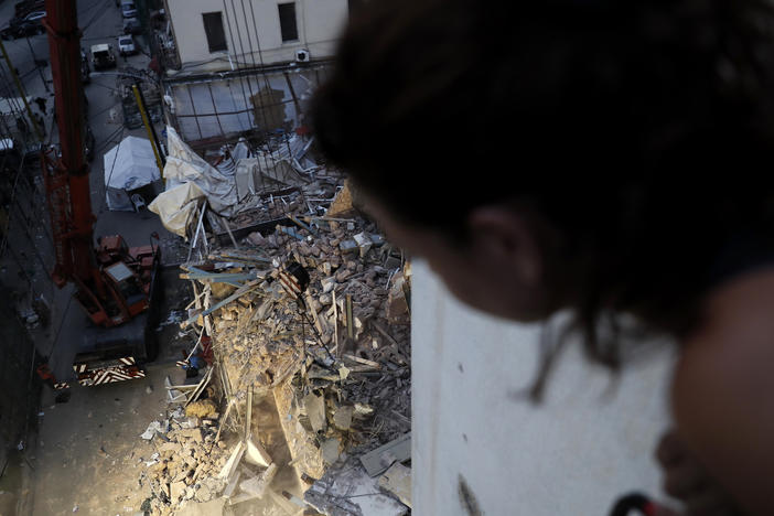 A woman watches from her apartment balcony as a crane removes the rubble of a building after a Chilean rescue team detected signals there may be a survivor at the site in Beirut, Lebanon, on Sept. 4, 2020.