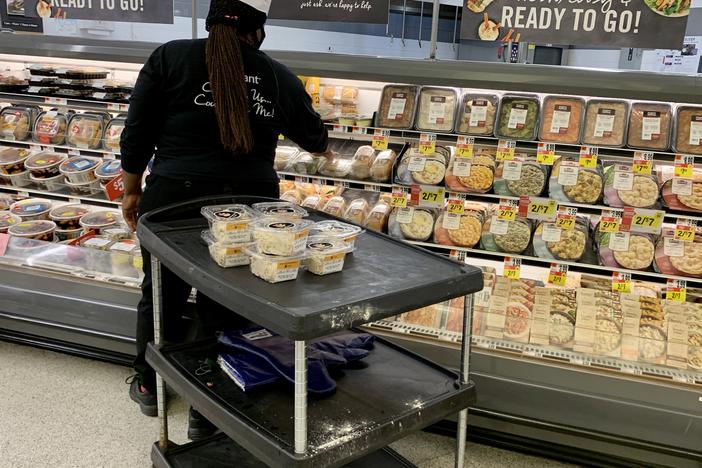 Grocery prices have fallen in recent months but are still 4.6% higher than at this time last year. Here, a woman stock shelves in a deli in June at a Washington, D.C., supermarket.