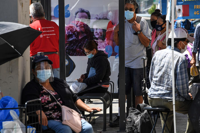 People wait for a bus in August in East Los Angeles. Latinos have the highest rate of labor force participation of any group in California — many in public-facing jobs deemed essential. That work has put them at higher risk of catching the coronavirus.